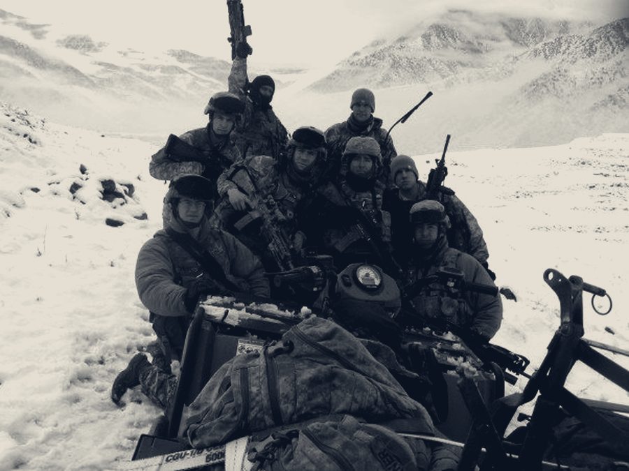 A squad of soldiers gathered around a vehicle in deep snow on a high mountain slope.